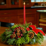 Christmas centerpiece with pine cones, gold balls and red berries with red velveteen bows and a red taper candle 