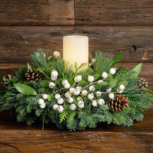 Centerpiece made of noble fir, pine, cedar and bay leaf with white berry clusters, Australian pine cones and 1 white LED pillar candle close up