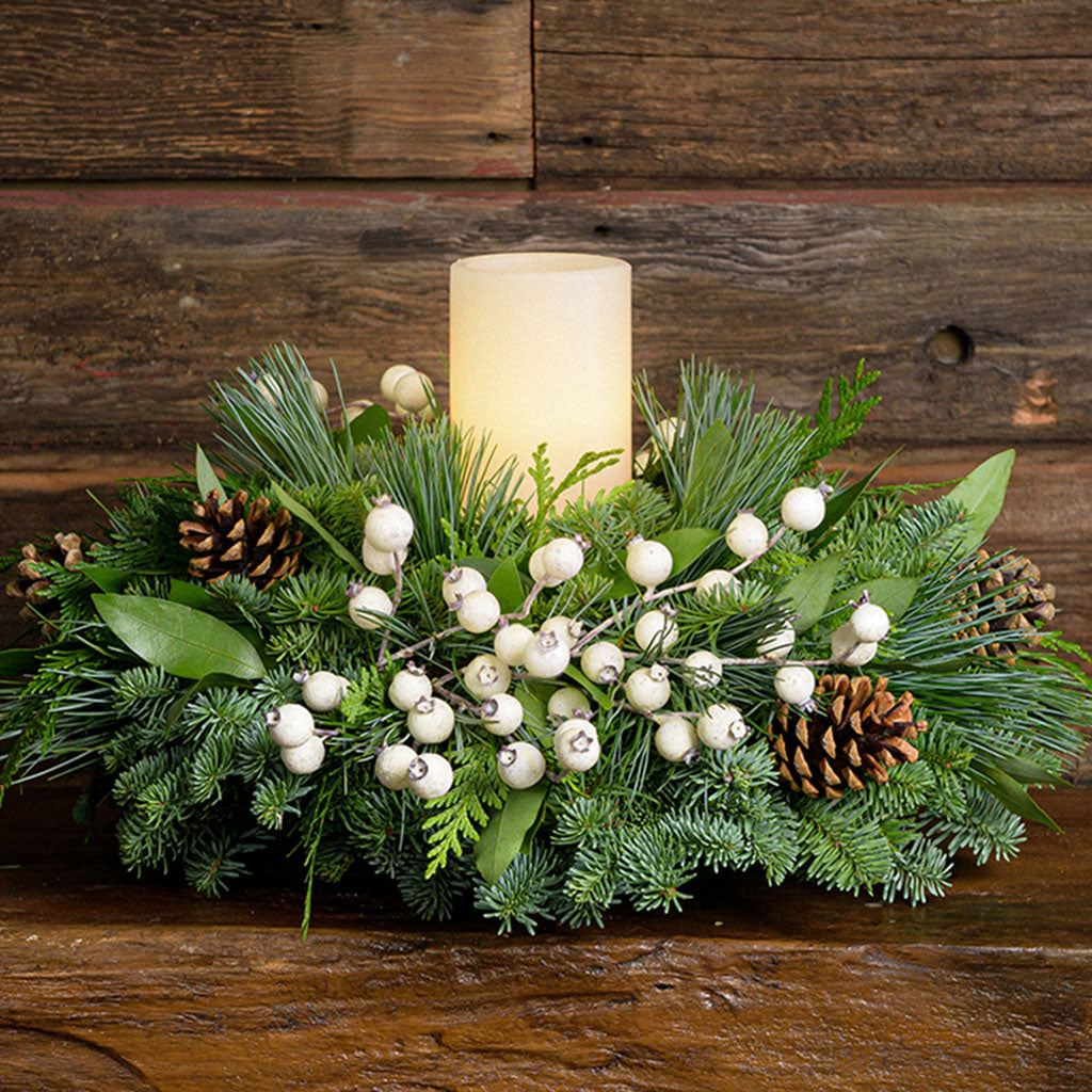 Centerpiece made of noble fir, pine, cedar and bay leaf with white berry clusters, Australian pine cones and 1 white LED pillar candle close up