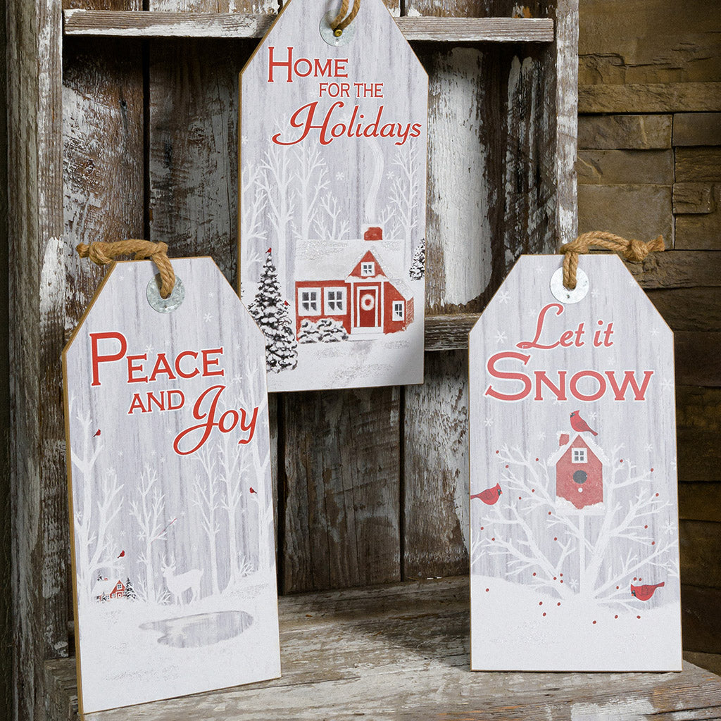 Set of 3 farmhouse grey-washed finish signs made of sturdy wood and hangs from a thick rustic jute rope. One sign says "Home for the Holidays" with red barn in a wintery holiday snow scene accented with trees. A second sign says "Peace and Joy" with snowy trees, birds, and a peaceful deer. The third sign says "Let it Snow" with cardinals birds visiting a sweet birdhouse all sitting on a shelf.