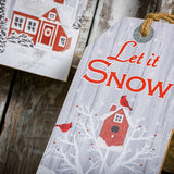 Close up Set of 3 farmhouse grey-washed finish signs made of sturdy wood and hangs from a thick rustic jute rope. One sign says "Home for the Holidays" with red barn in a wintery holiday snow scene accented with trees. A second sign says "Peace and Joy" with snowy trees, birds, and a peaceful deer. The third sign says "Let it Snow" with cardinals birds visiting a sweet birdhouse all sitting on a shelf.