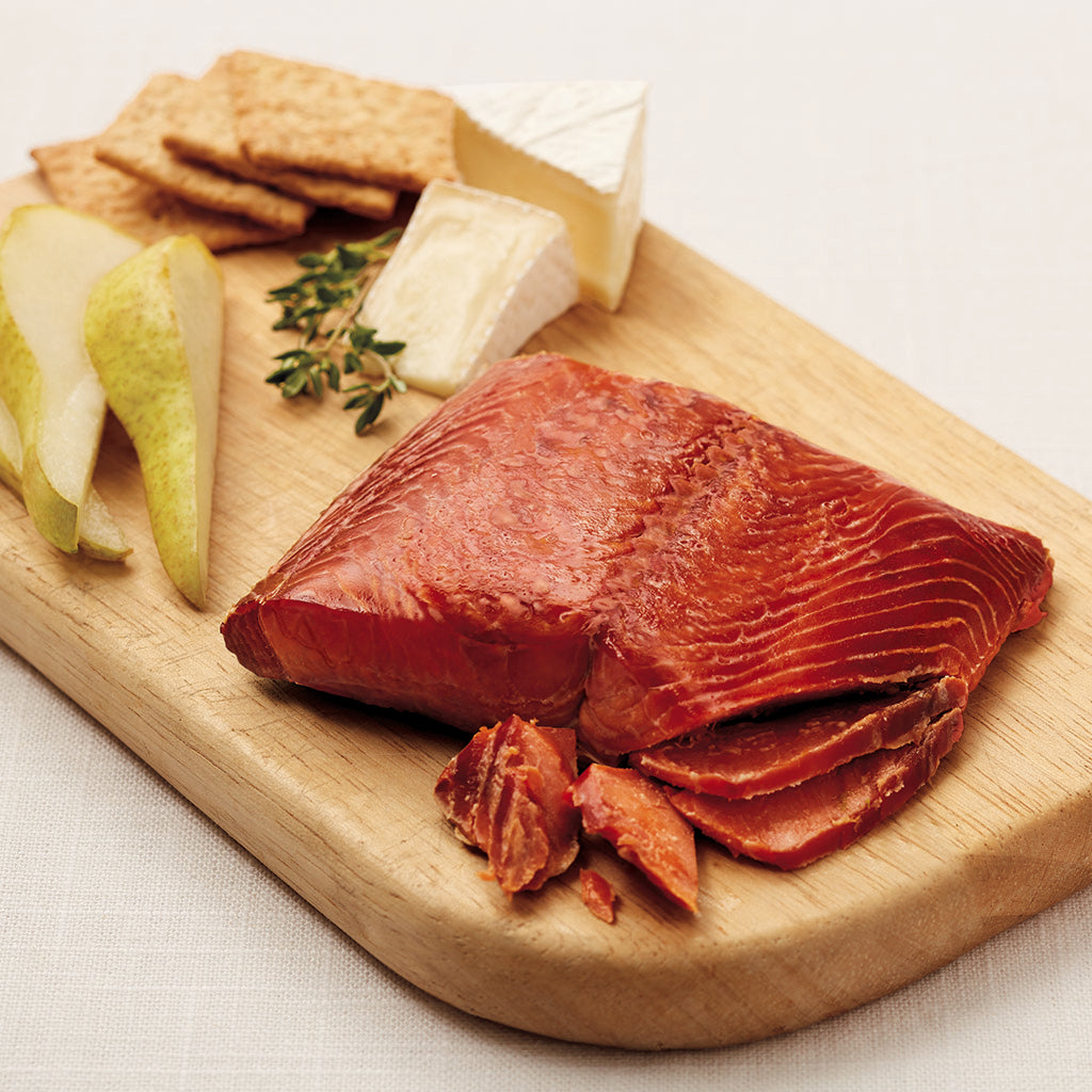 Smoked salmon with crackers, cheese, and a green pears sitting on a wooden cutting board.