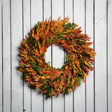 22" wreath made of naturally preserved green, yellow, and orange myrtle on a white wood fence background. 