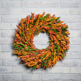 22" wreath made of naturally preserved green, yellow, and orange myrtle on a white brick background. 
