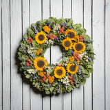 22" floral wreath made of  eucalyptus, yellow coxcomb, white statice, red globe amaranthus, salal leaves, and real sunflowers on a white wood fence background.