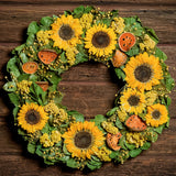 A close-up of a dried wreath made of preserved sunflowers, dried citrus quince slices, natural yarrow, and natural yellow flax pods on a base of natural lemon leaves hung on a dark wood background.