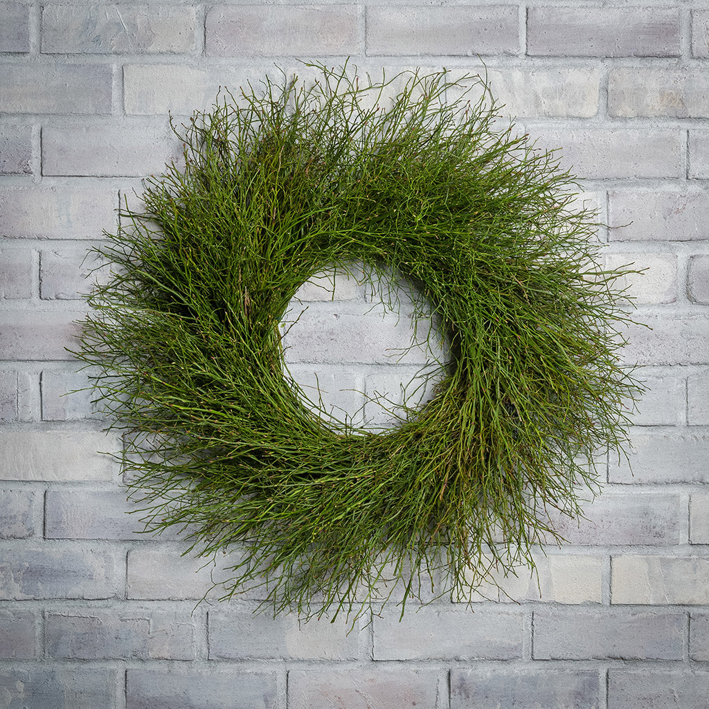 A wreath of sweet huckleberry branches hanging on a white brick wall. 