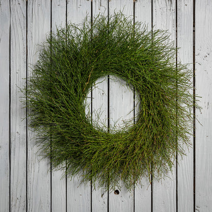 A wreath of sweet huckleberry branches hanging on a white wood fence.