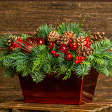 Centerpiece made of noble fir, cedar, and pine with Australian pine cones, red berry clusters, apple/pine cone picks, and a red metallic container