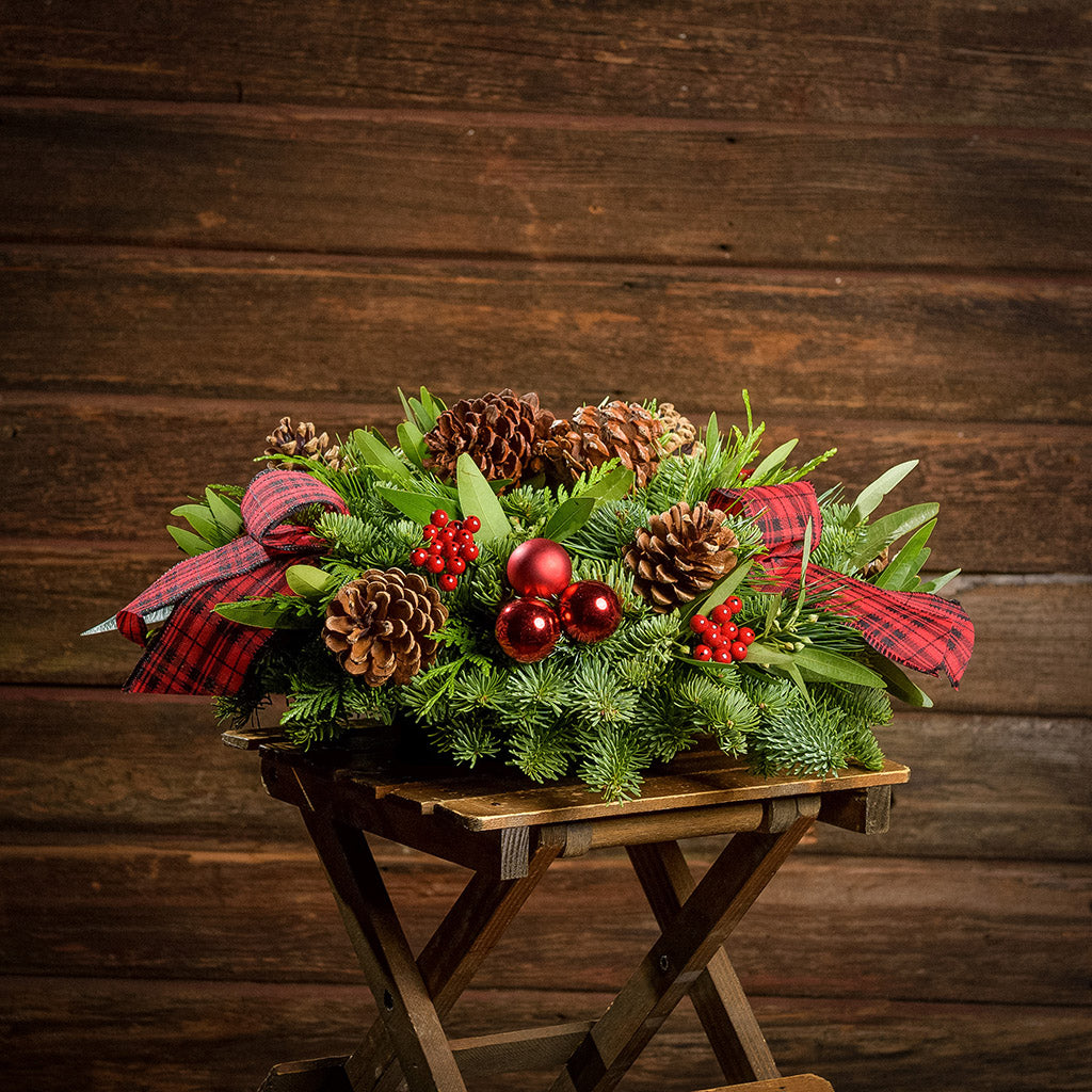 Holiday centerpiece with pine cones, red balls and red and black tartan bows with a dark wooden background.