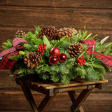 Holiday centerpiece with pine cones, red balls and red and black tartan bows with a dark wooden background.