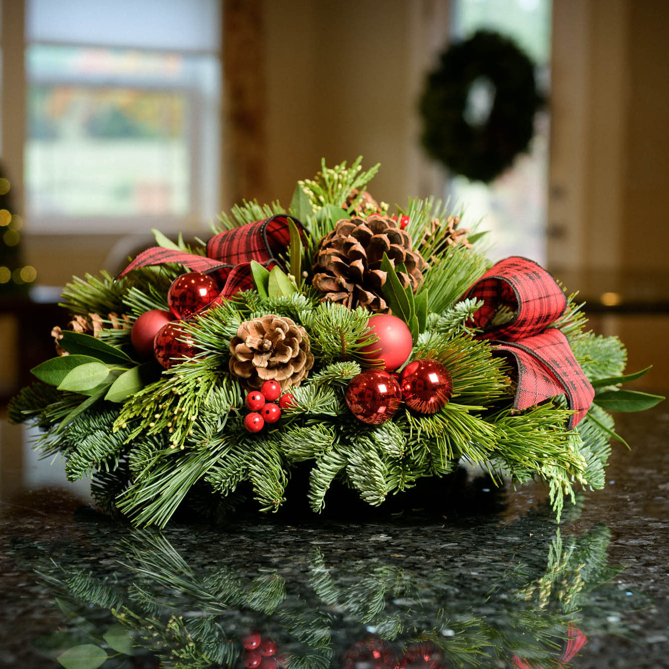 Holiday centerpiece with pine cones, red balls and red and black tartan bows sitting on a kitchen counter