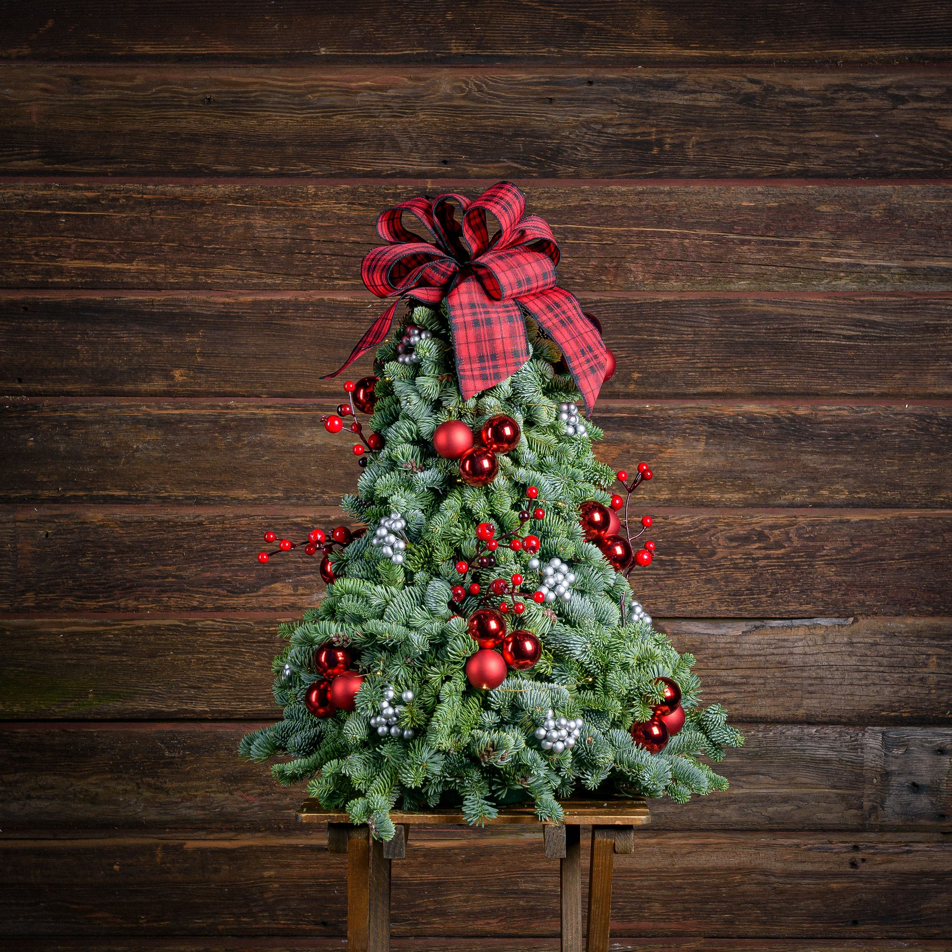 Assembled tree of noble fir,red ornaments, silver berries, red berry branch and a red and black tartan bow