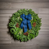 Christmas wreath made of fir, pine, cedar and juniper with pine cones and a blue brushed-linen bow on a wooden background.