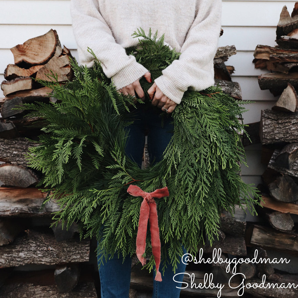 Christmas wreath with cedar and pine held by a person.