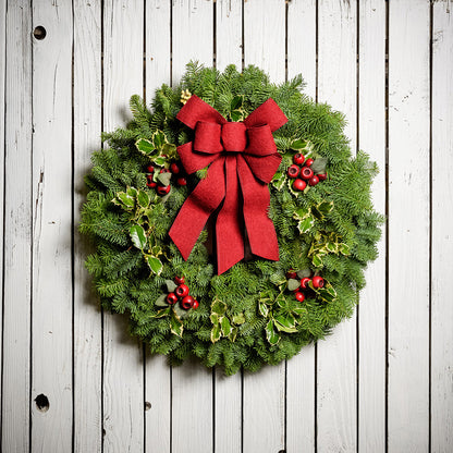 Christmas wreath made of noble fir and variegated holly with 4 country-berry clusters and a red brushed-linen bow on a white wood background.