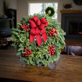 Christmas wreath made of noble fir and variegated holly with 4 country-berry clusters and a red brushed-linen bow on a wreath stand on a tabletop