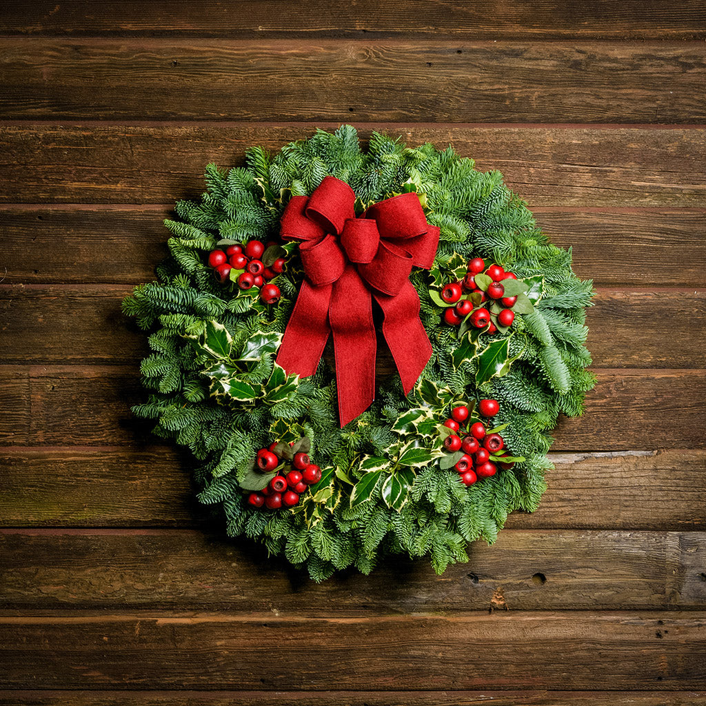 Christmas wreath made of noble fir and variegated holly with 4 country-berry clusters and a red brushed-linen bow