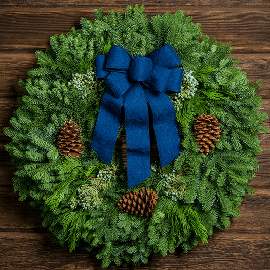 Christmas wreath made of fir, pine, cedar and juniper with pine cones and a blue brushed-linen bow on a wooden background.