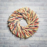 22" wreath made of red and blue oats and natural corn husk on a white brick background.