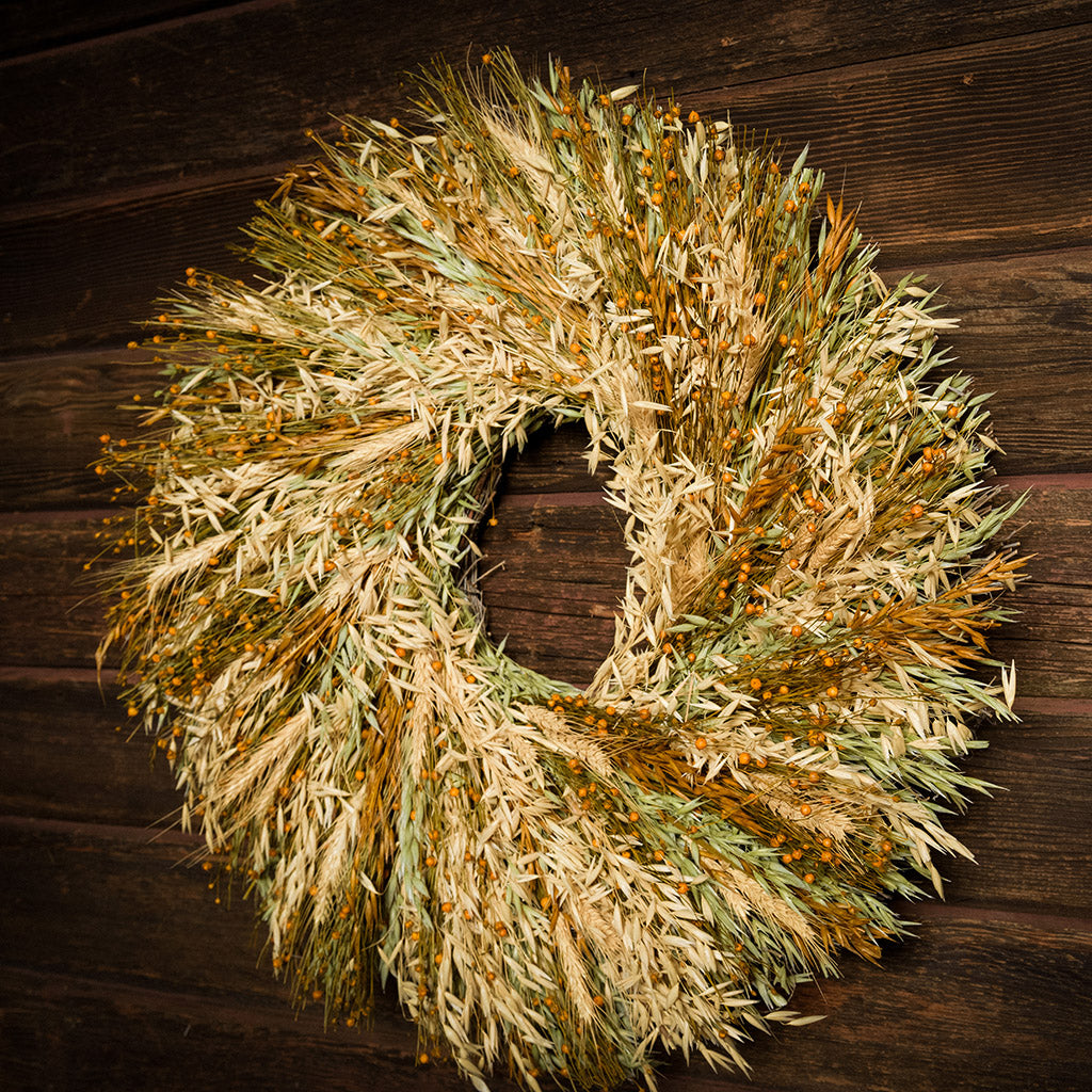 A wreath made of Sunkissed Aveena-oats, dijon Sudan grass, saffron flax, and natural wheat on a dark wood background.