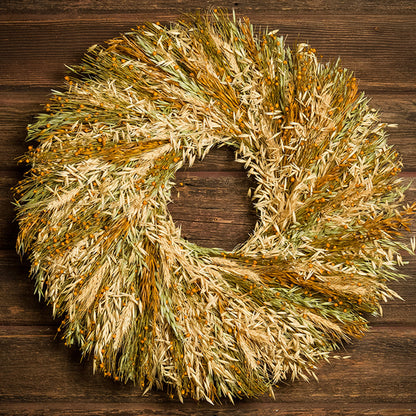 A wreath made of Sunkissed Aveena-oats, dijon Sudan grass, saffron flax, and natural wheat on a dark wood background.