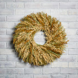 A wreath made of Sunkissed Aveena-oats, dijon Sudan grass, saffron flax, and natural wheat on a white brick background.