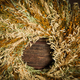 A wreath made of Sunkissed Aveena-oats, dijon Sudan grass, saffron flax, and natural wheat on a dark wood background.