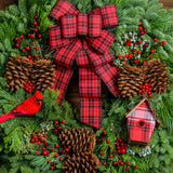 Holiday wreath made of noble fir, white pine, incense cedar, and juniper with ponderosa pine cones, red rosehip/mini pine cone clusters, faux berry clusters, red cardinal, a mini plaid birdhouse, and a red and black plaid bow close up