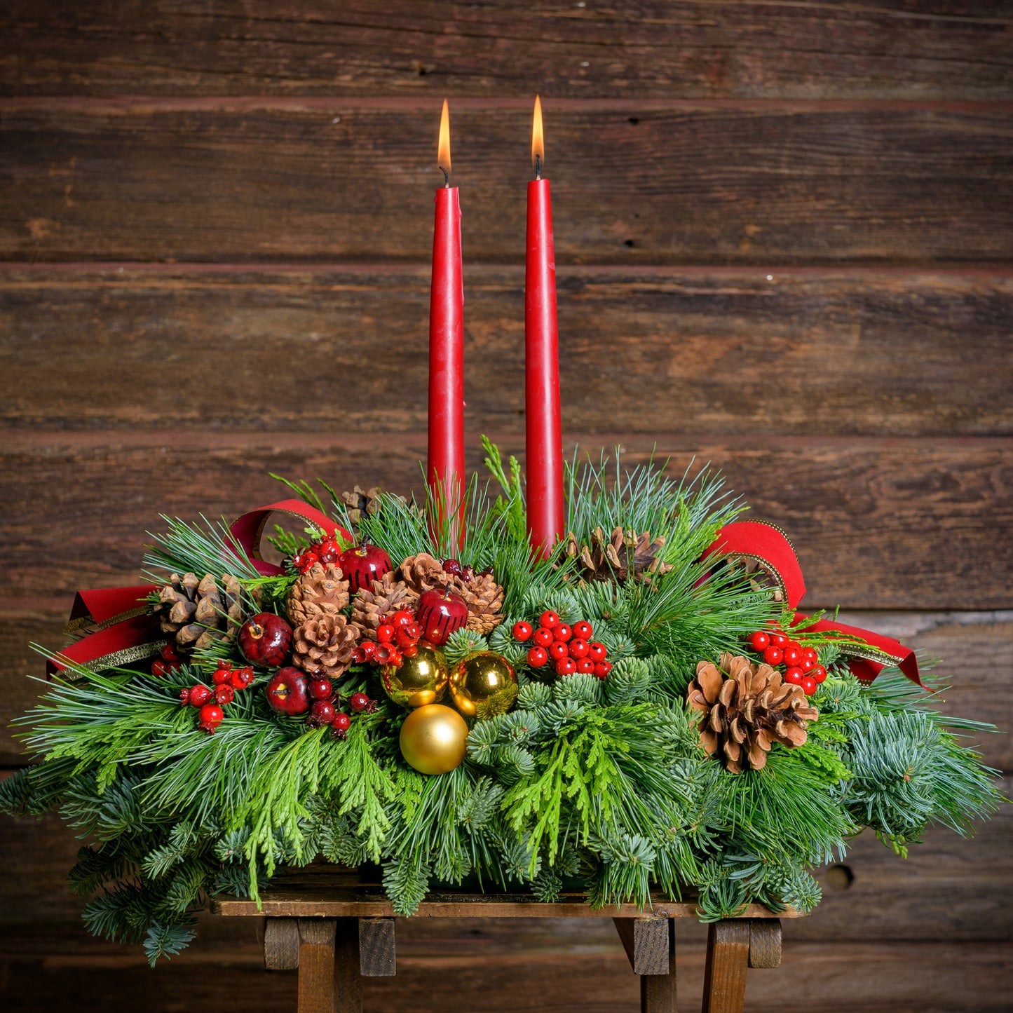 Traditional centerpiece with red balls, pine cones and berries with 2 red velveteen bows and two red taper candles 