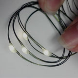 White LED lights on a thin green wire near a thumb for scale